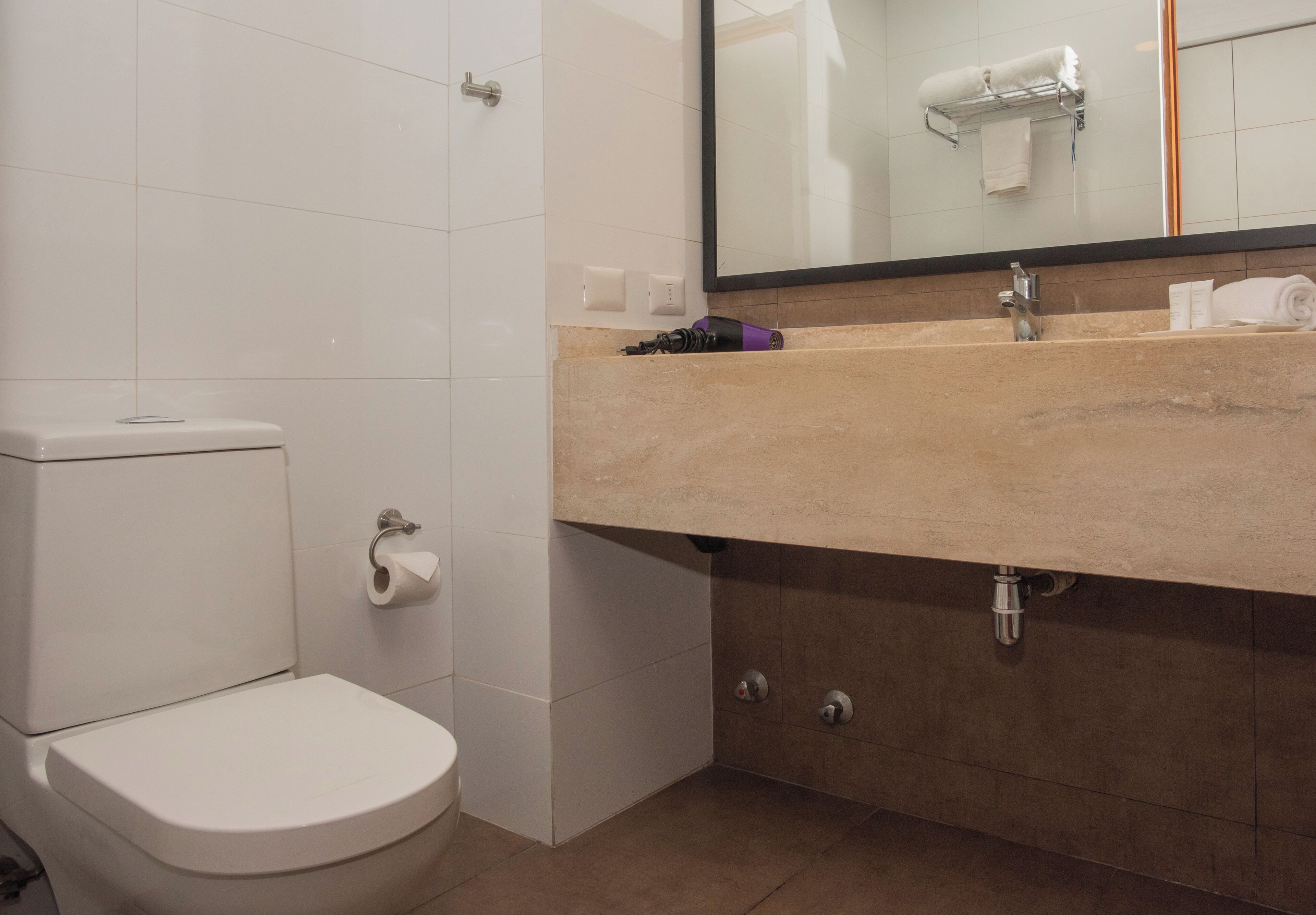 A bathroom with a toilet, sink, mirror, and towel rack.