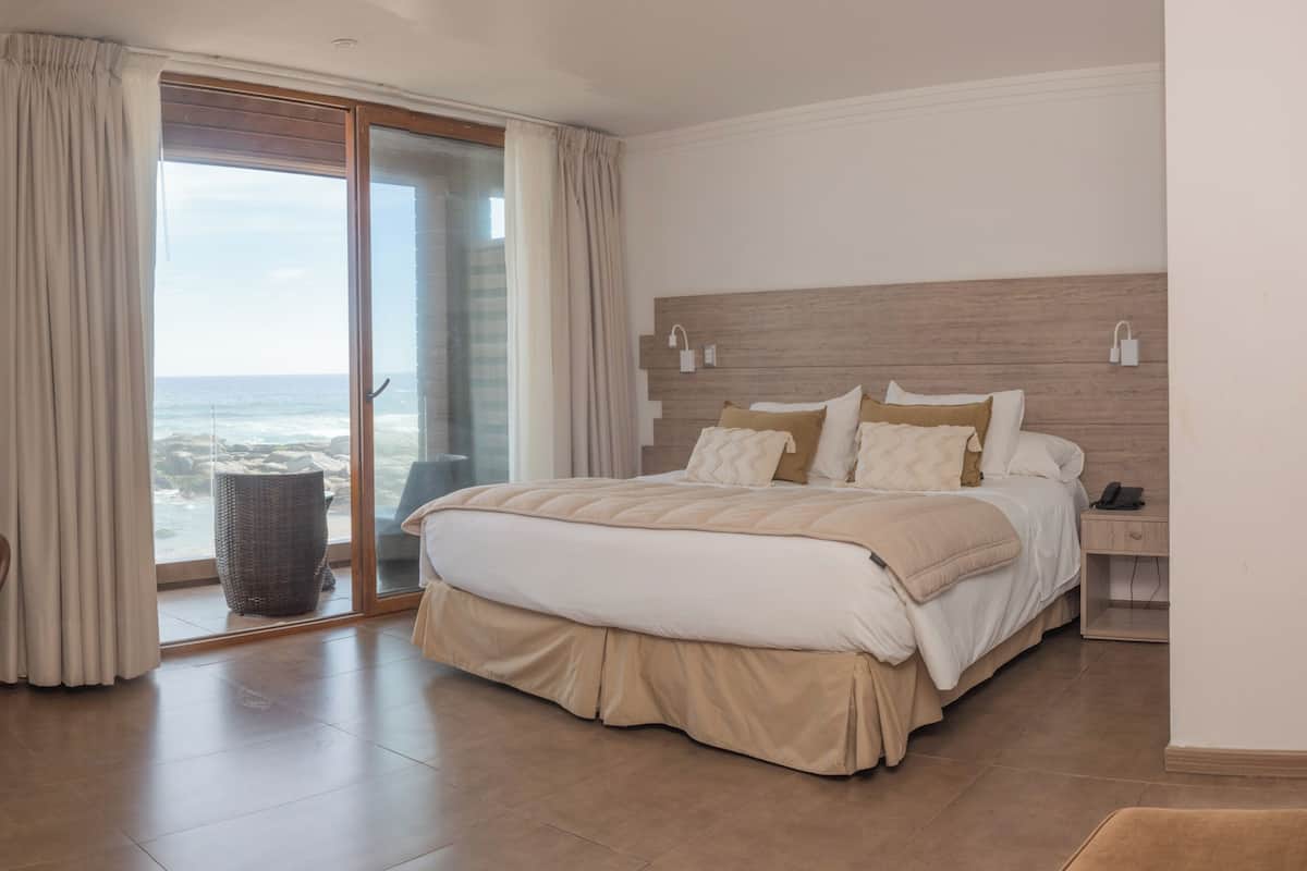 Un dormitorio con cama, una silla, una mesa, un televisor y vista al océano.