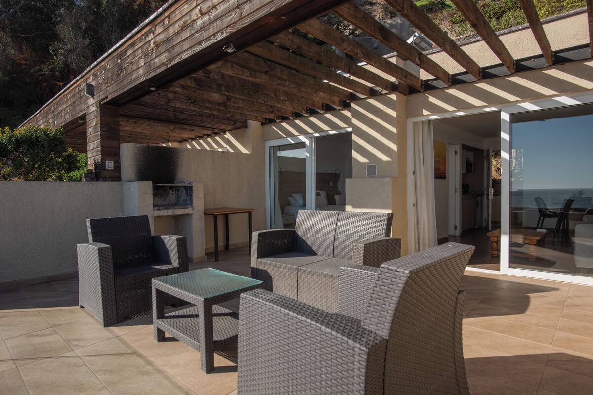 Un espacio al aire libre con patio, mobiliario de mimbre, una mesa de vidrio y vista al mar.