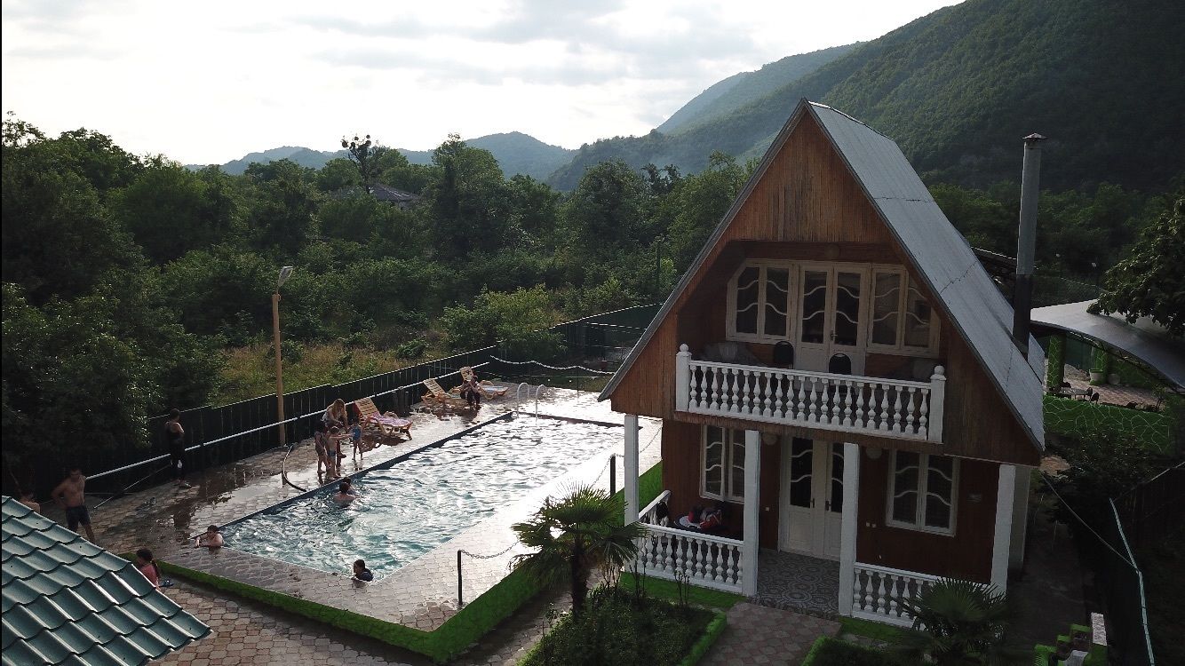 Una casa de madera con balcón, piscina y montañas al fondo.