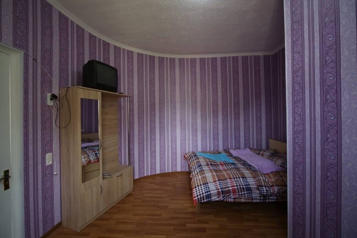 A bedroom with a bed, a wooden wardrobe, and a television on top.