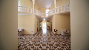 A spacious hallway with patterned flooring, a balcony with a white balustrade, and a staircase leading to an upper level. - Hotel Canyon (Khoni)