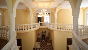 A grand hallway with a white balustrade, a chandelier, and a fireplace. - Hotel Canyon (Khoni)