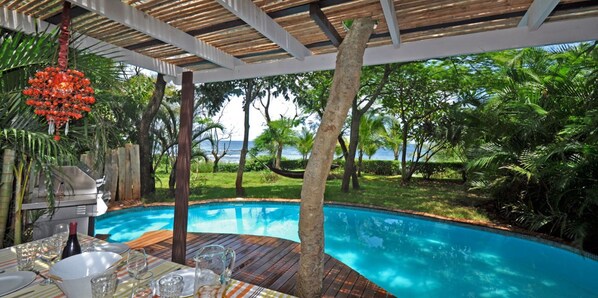 A poolside area with a wooden deck, a grill, and a view of the ocean.