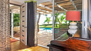 Habitación con piso de madera, un piano y vista a una piscina y mobiliario exterior.