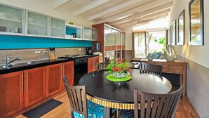 Una cocina moderna con comedor, que cuenta con una isla central con un felpudo verde y flores rojas, armarios de madera y encimera negra.