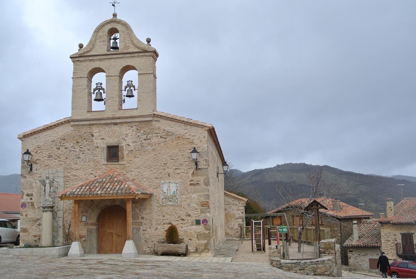 Una chiesa storica in pietra con un campanile, un portale in legno e una piccola campana.
