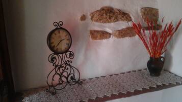 Un reloj de pared, un florero con detalles decorativos rojos y un encaje sobre una repisa.