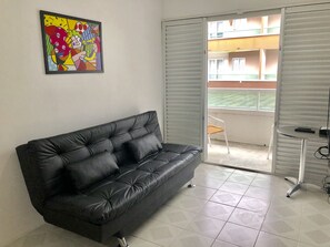 Relax in this stylish living room with a sofa, abstract art, and sliding glass door leading to an outdoor area with a view.