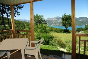 Une terrasse en bois avec une table et une chaise, d’où l’on a vue sur un lac et des montagnes.