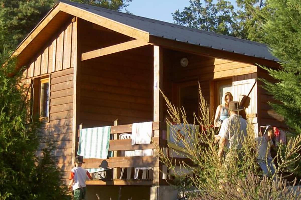 Een houten vakantiehuisje met een veranda, omringd door bomen.