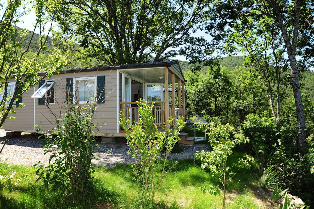 Een klein huisje met een veranda, omringd door weelderige begroeiing en bomen.