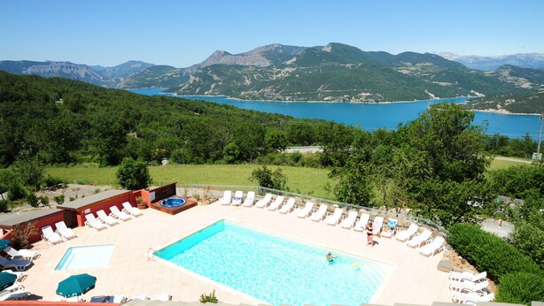 Un espace piscine doté de chaises longues et d’un jacuzzi, entouré d’une végétation luxuriante et avec des montagnes en toile de fond.