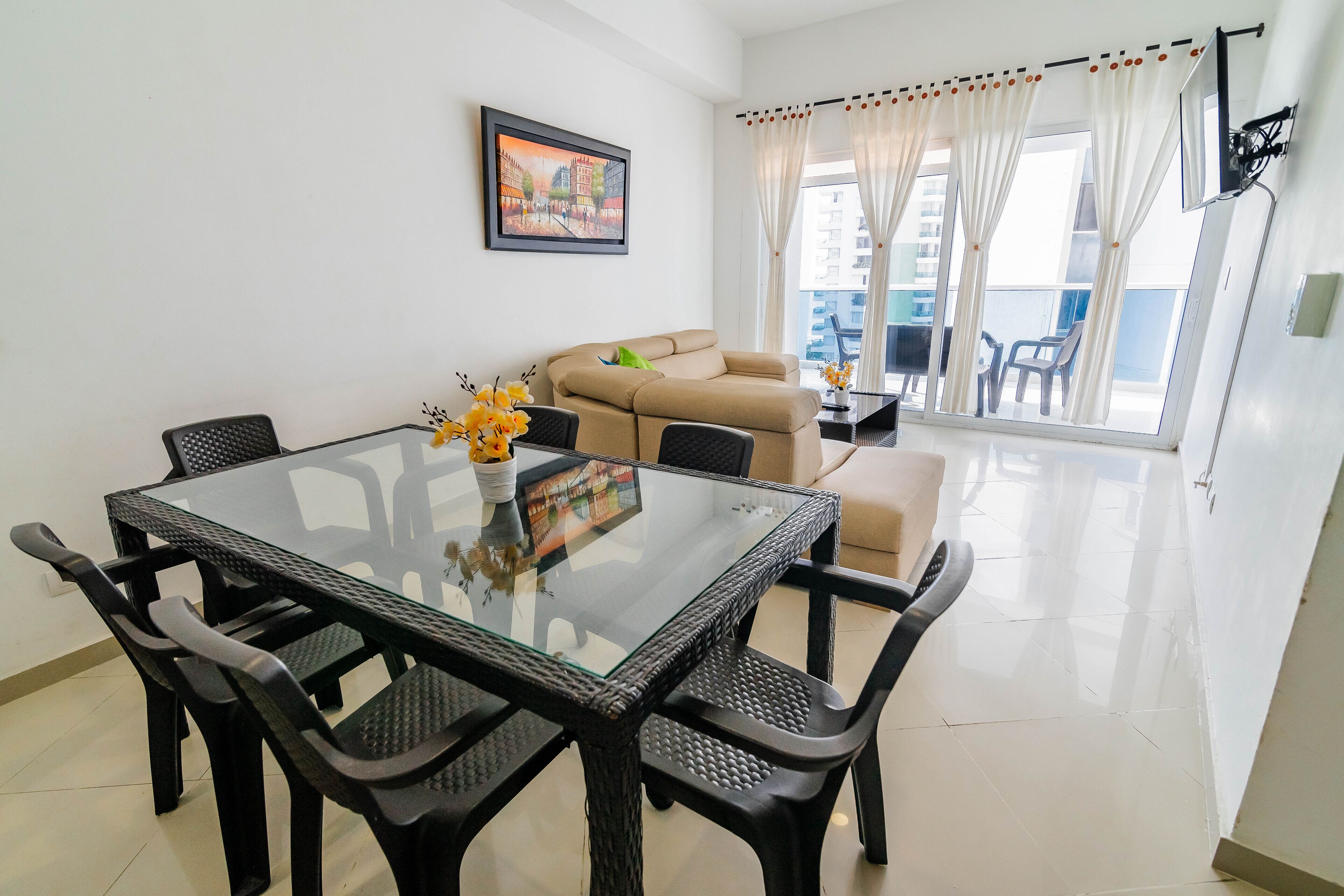Un coin repas avec une table à plateau en verre, des chaises noires et un canapé beige.