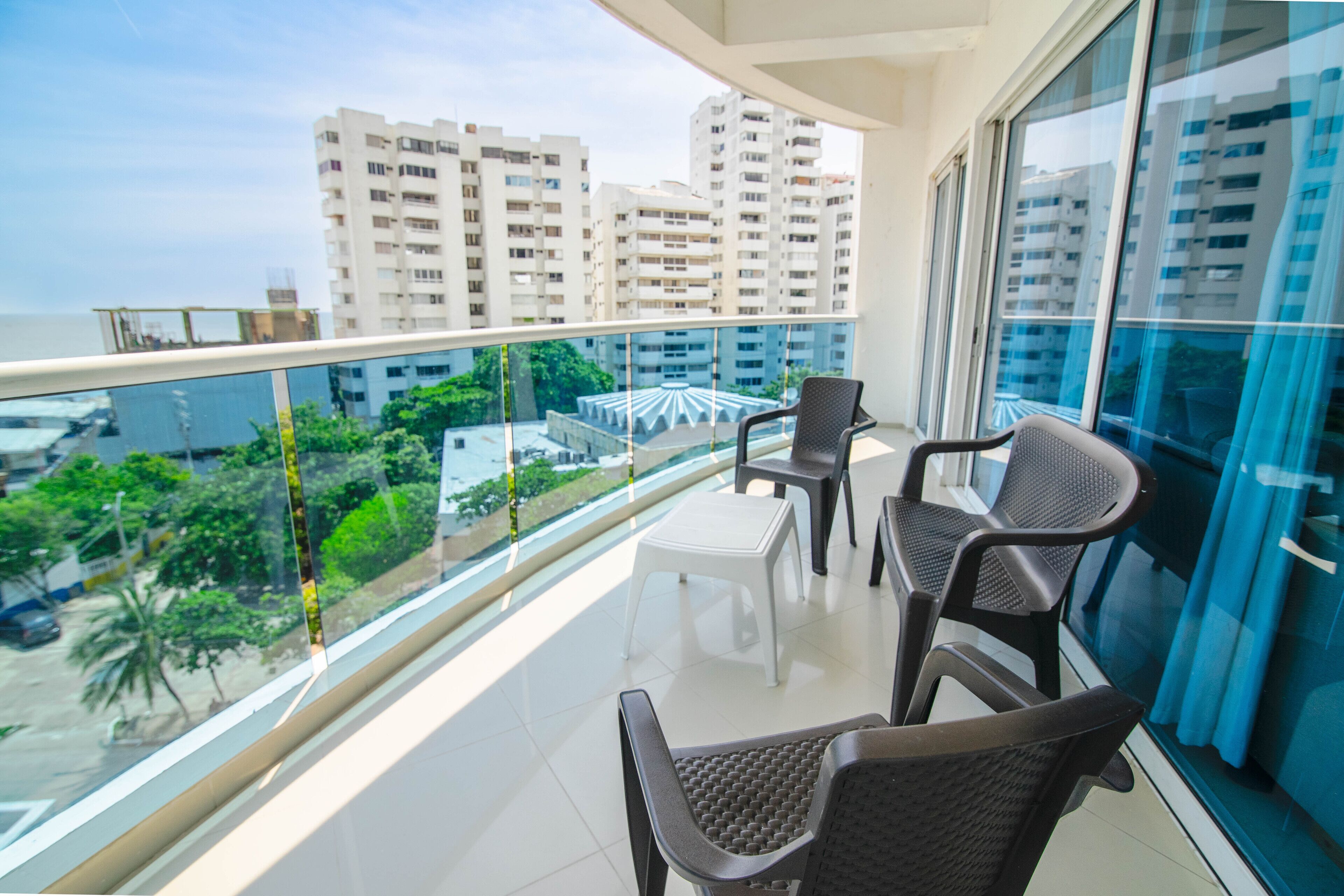 A balcony with two chairs and a small table, overlooking a cityscape with tall buildings and greenery.