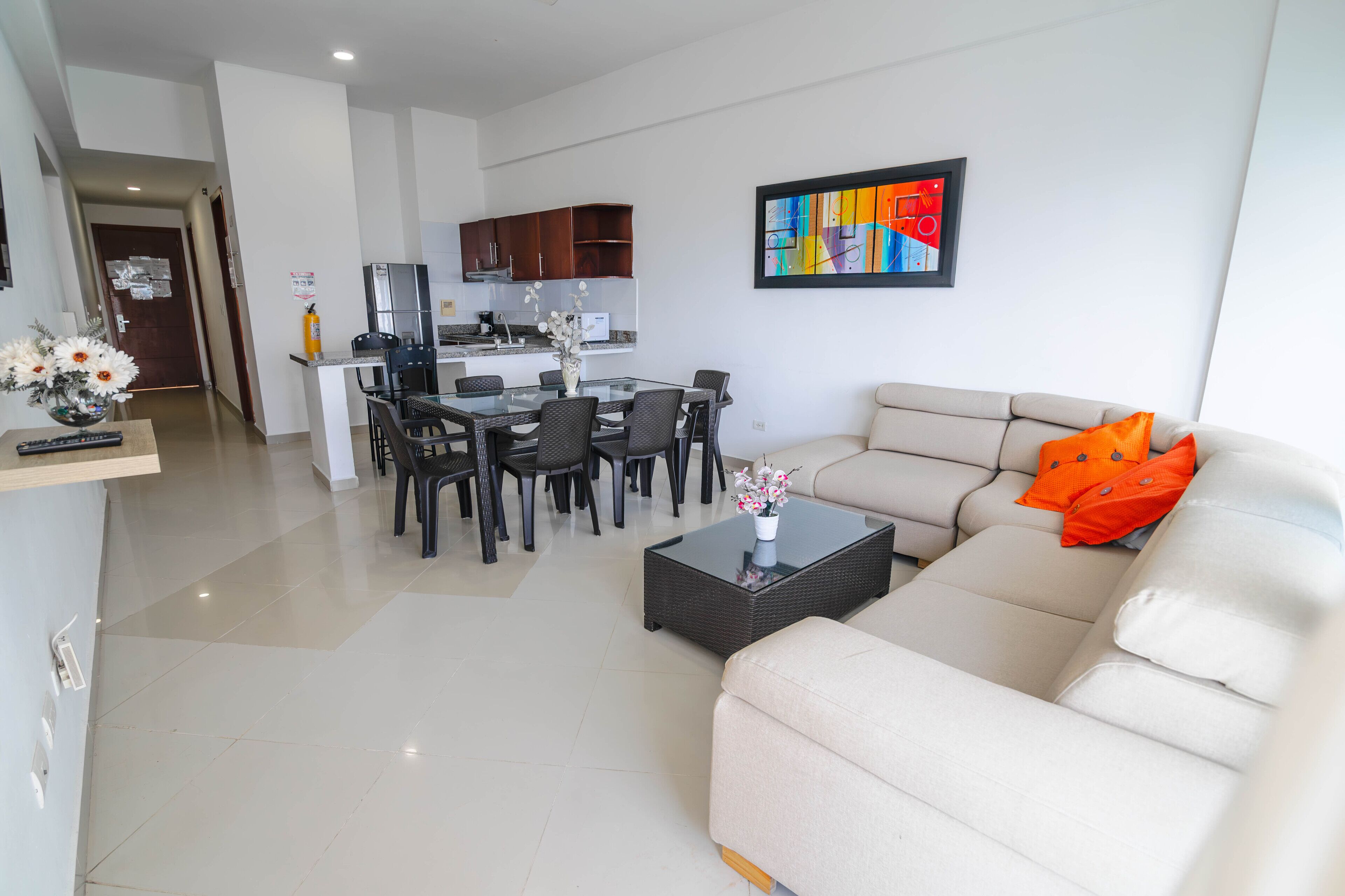 Uma sala de estar moderna com um sofá bege, uma mesa de centro de vidro e um espaço de jantar com uma mesa e cadeiras de vidro.