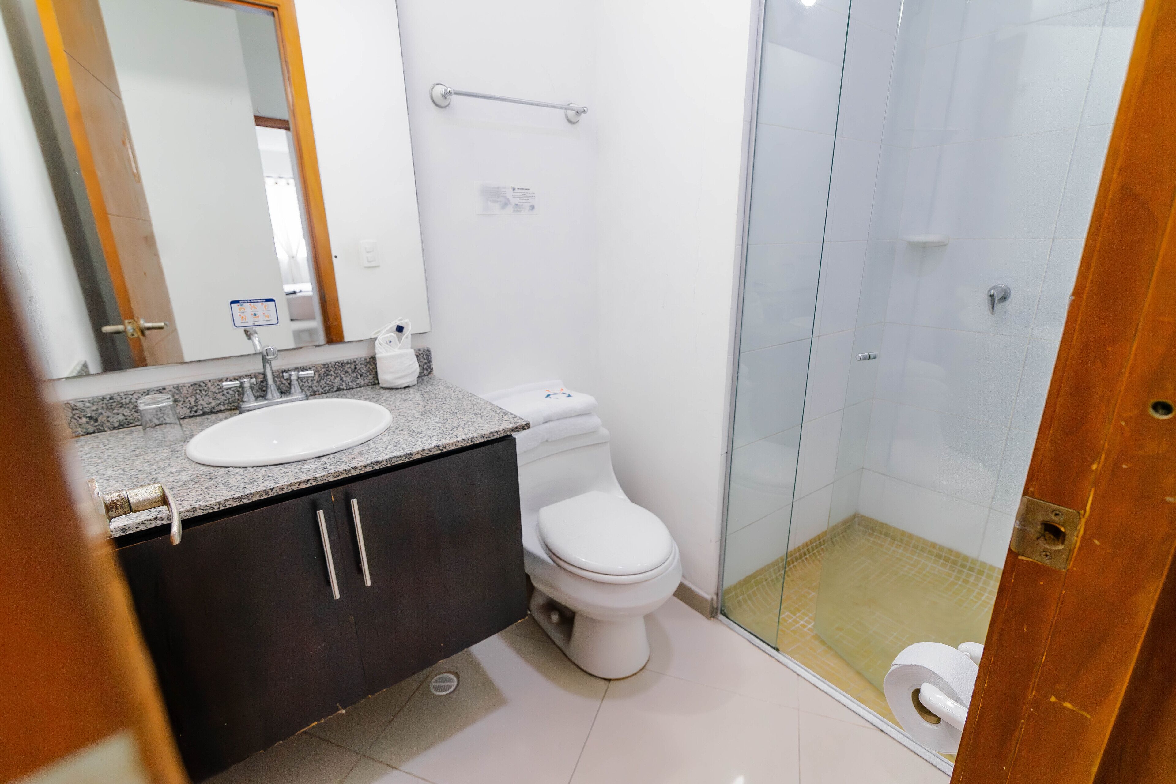 A modern bathroom with a granite countertop, a white sink, a toilet, and a glass-enclosed shower area.