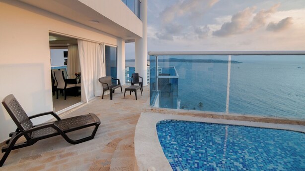 A balcony with a pool, chairs, and a view of the sea.