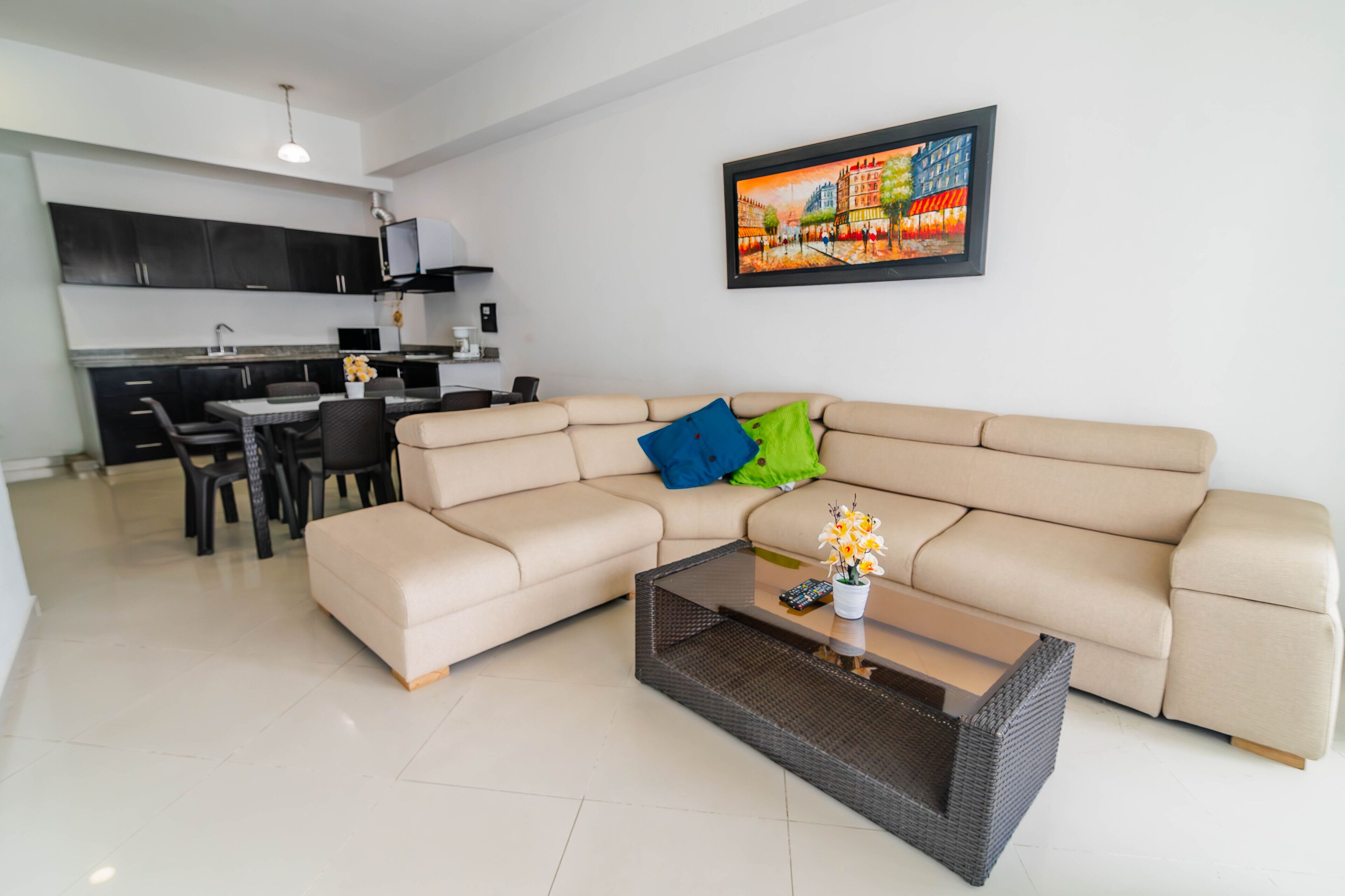 A modern living room with a beige sectional sofa, a glass coffee table, and a dining area with a black table and chairs.