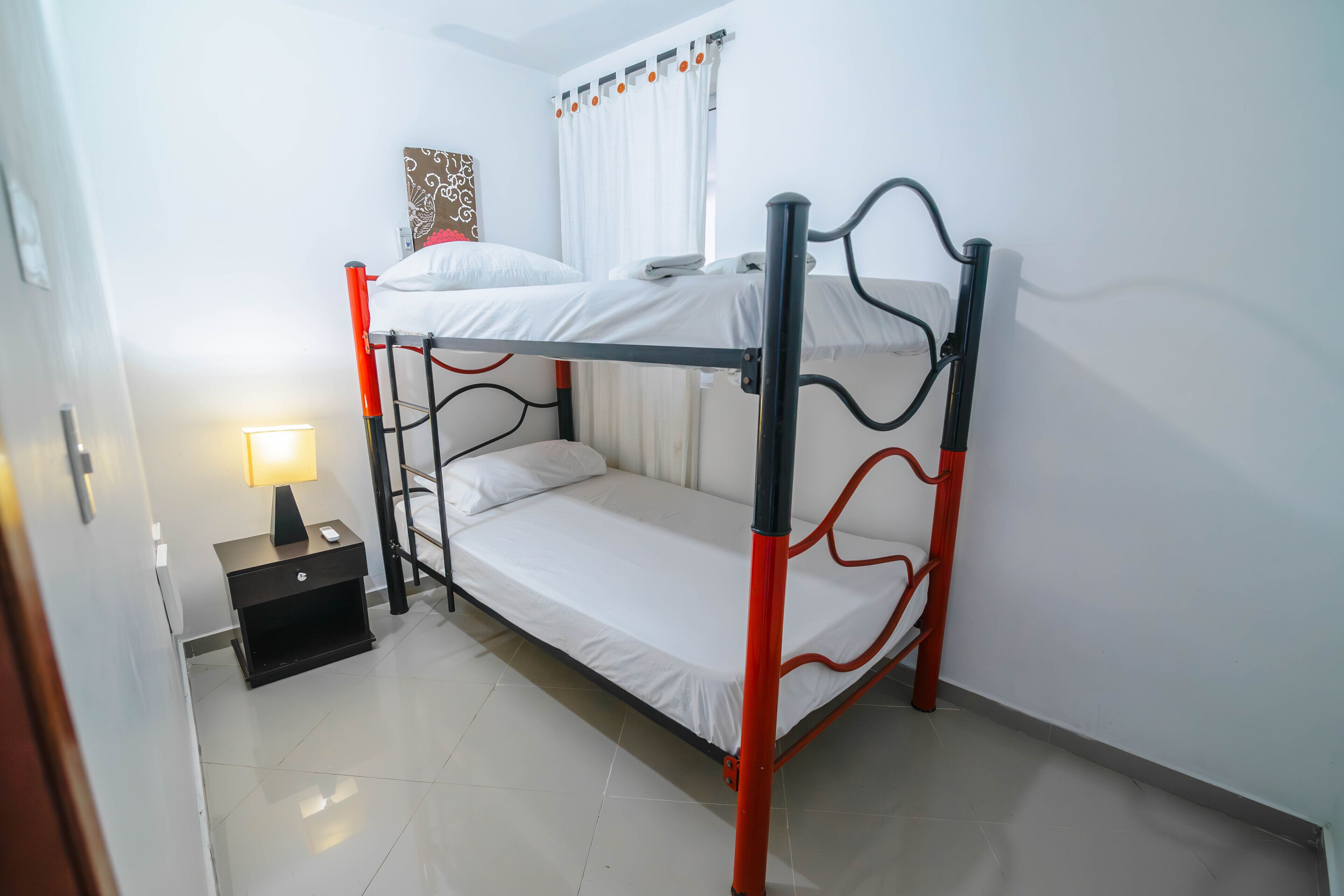 Dormitorio con literas, mesita de noche, lámpara y cortina.