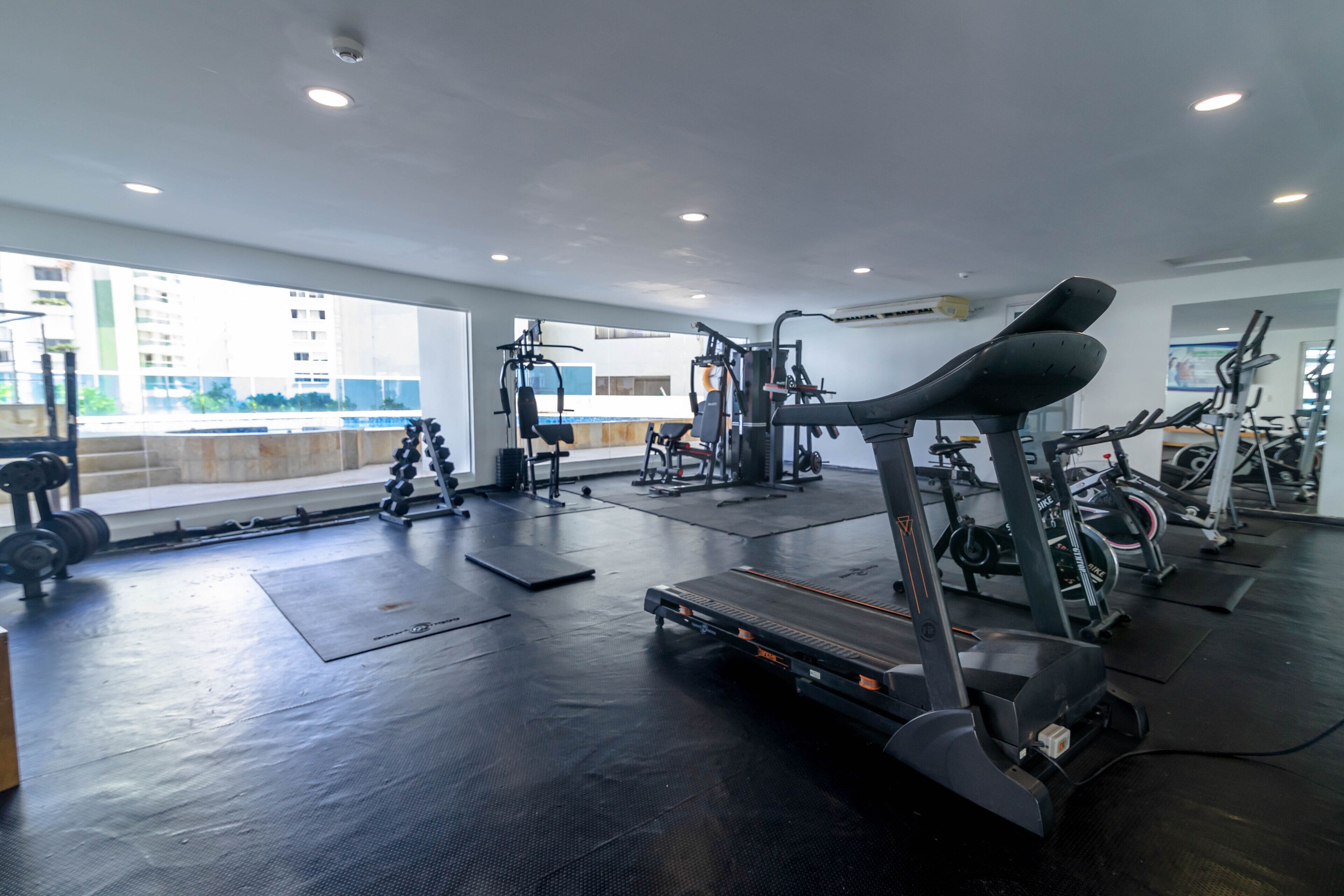 Une salle de sport équipée de tapis de course, d’appareils de musculation et de poids libres.