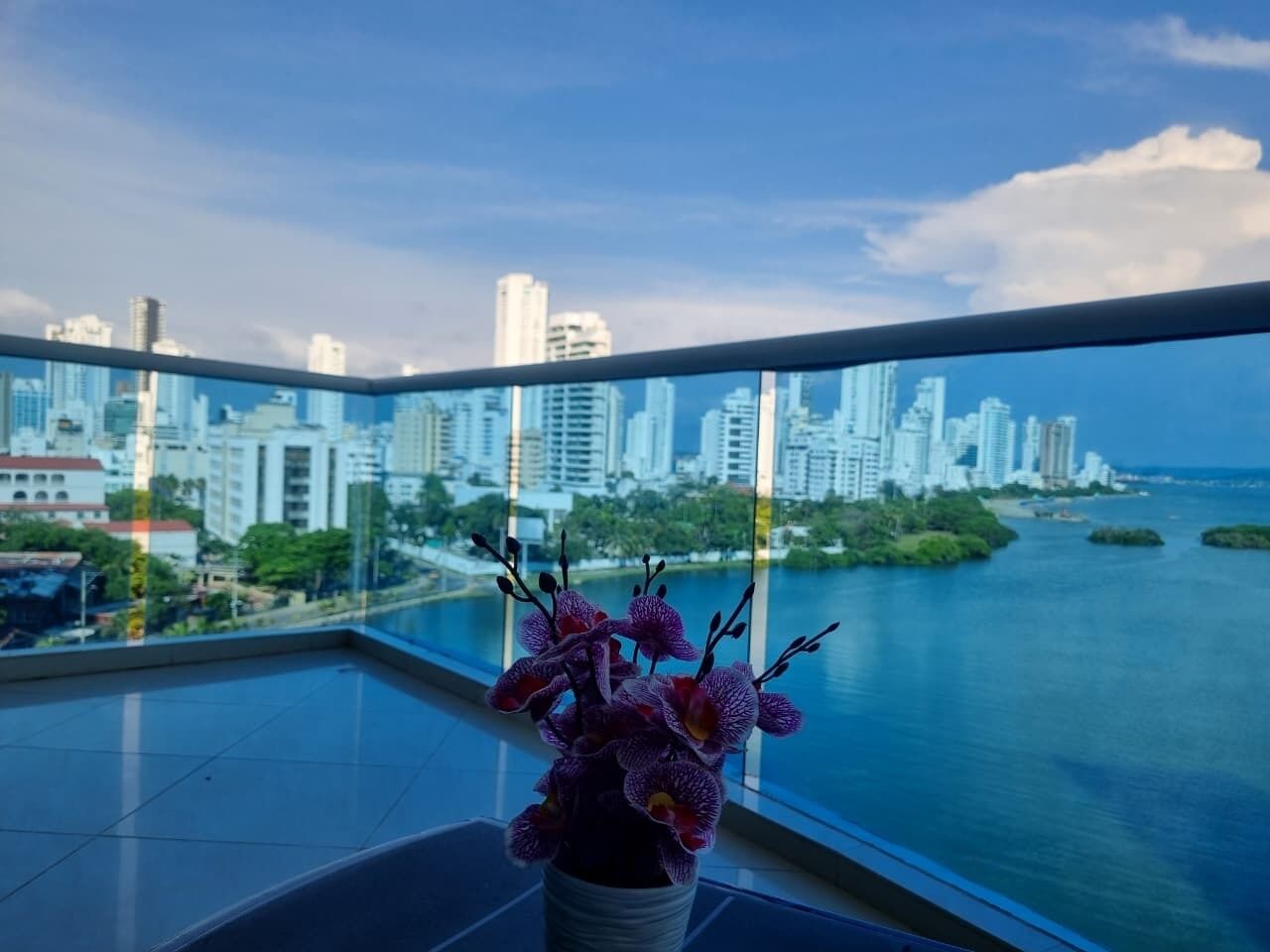 Un balcon offrant une vue sur les gratte-ciel d’une ville et sur une étendue d’eau.
