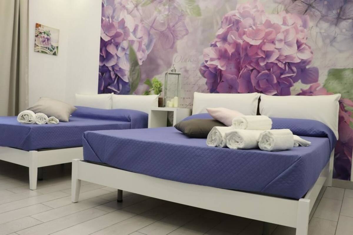 Habitación de hotel con dos camas, cada una con cubrecama azul y cabeceros blancos. Hay toallas enrolladas sobre cada cama.