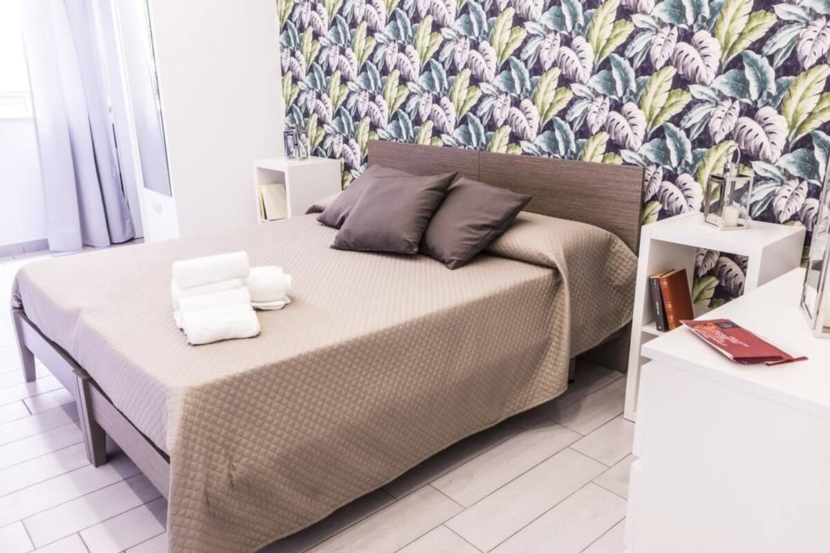 Una cama bien hecha con un edredón color beige, dos almohadas y un juego de toallas blancas.
