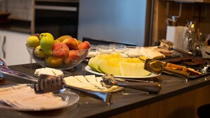 A buffet table with various fruits, cheese, and utensils.