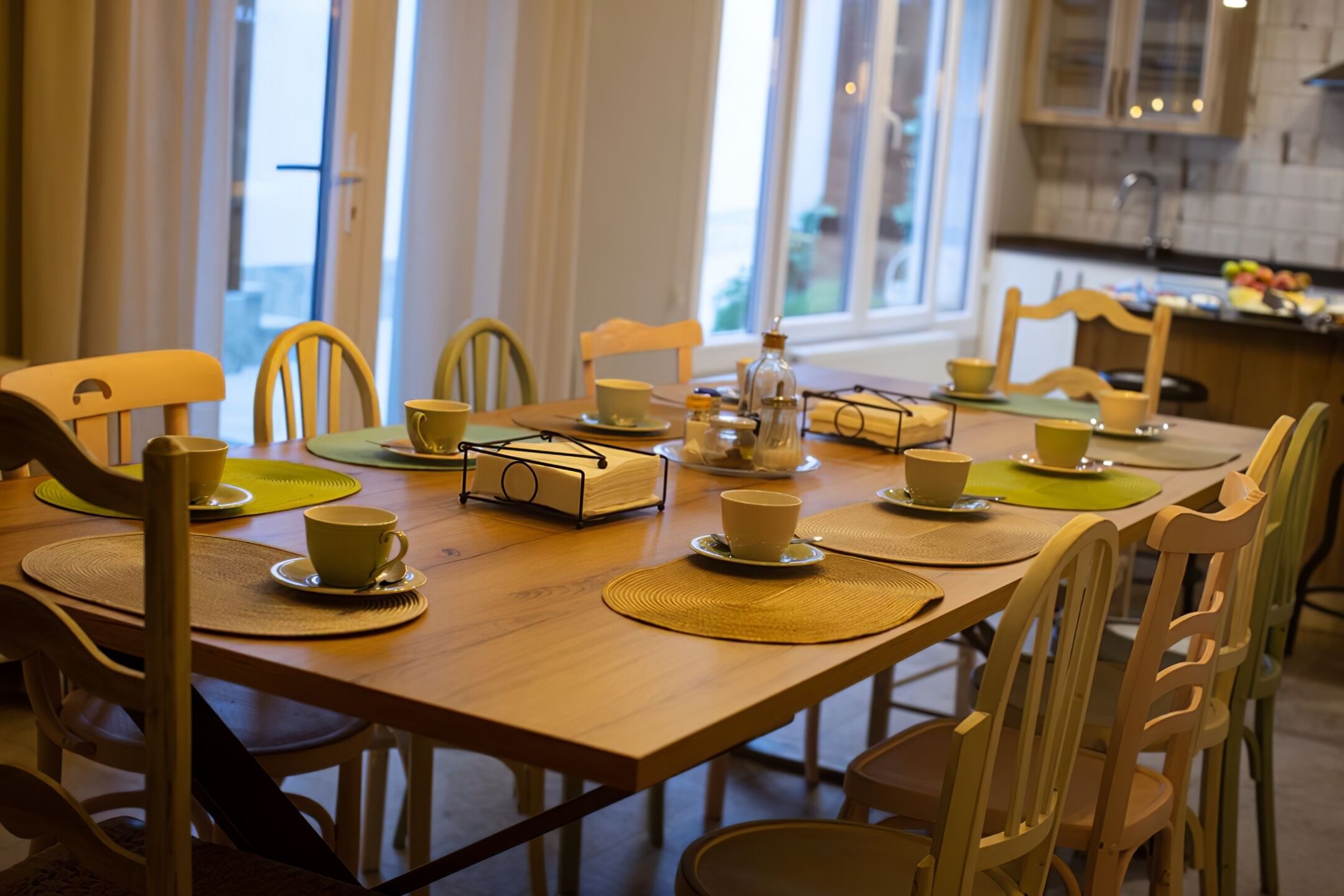 A dining table set with yellow chairs, placemats, and white cups.