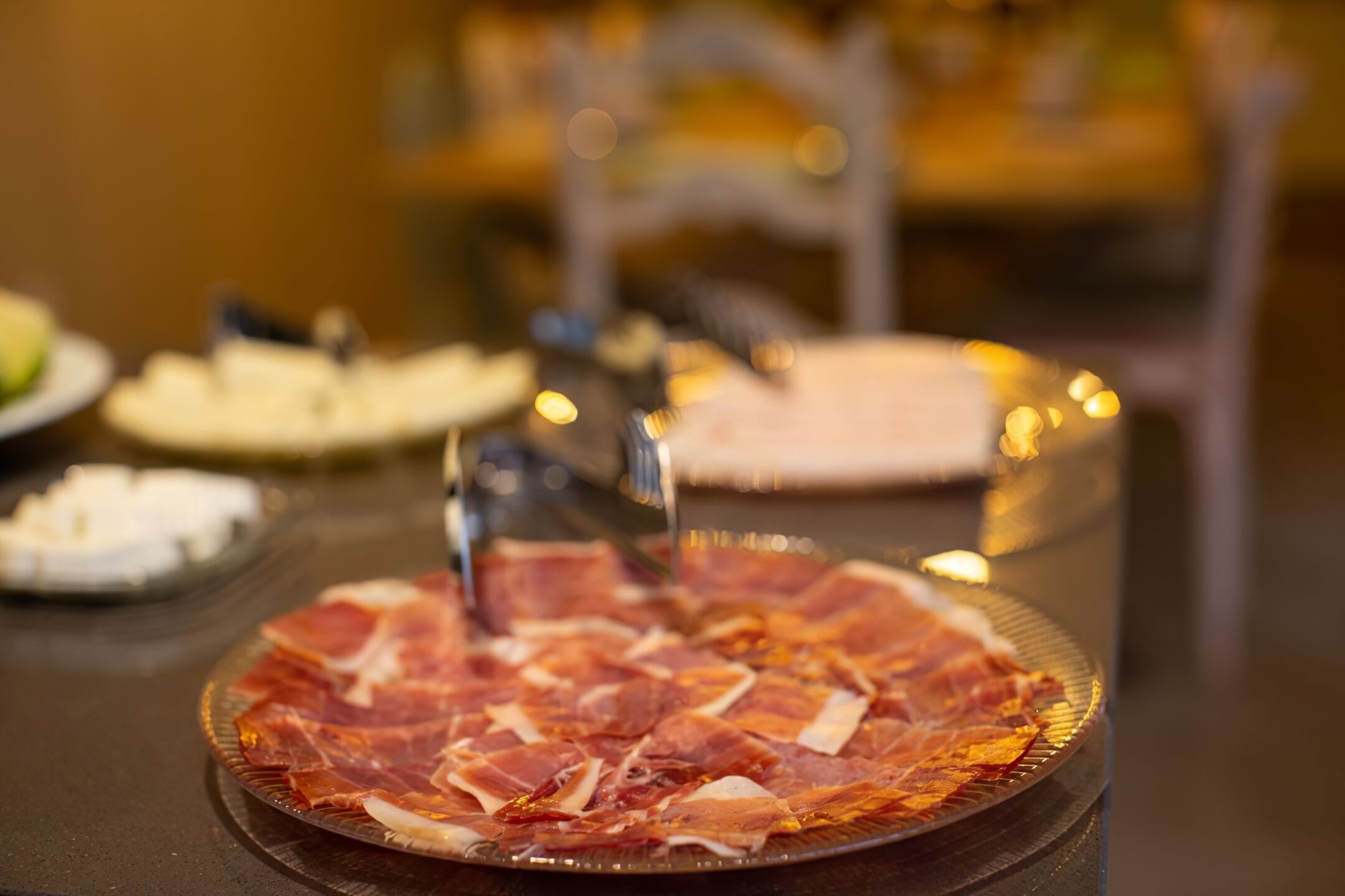Un plato de vidrio con carne en rodajas, un tenedor y una servilleta sobre una mesa.