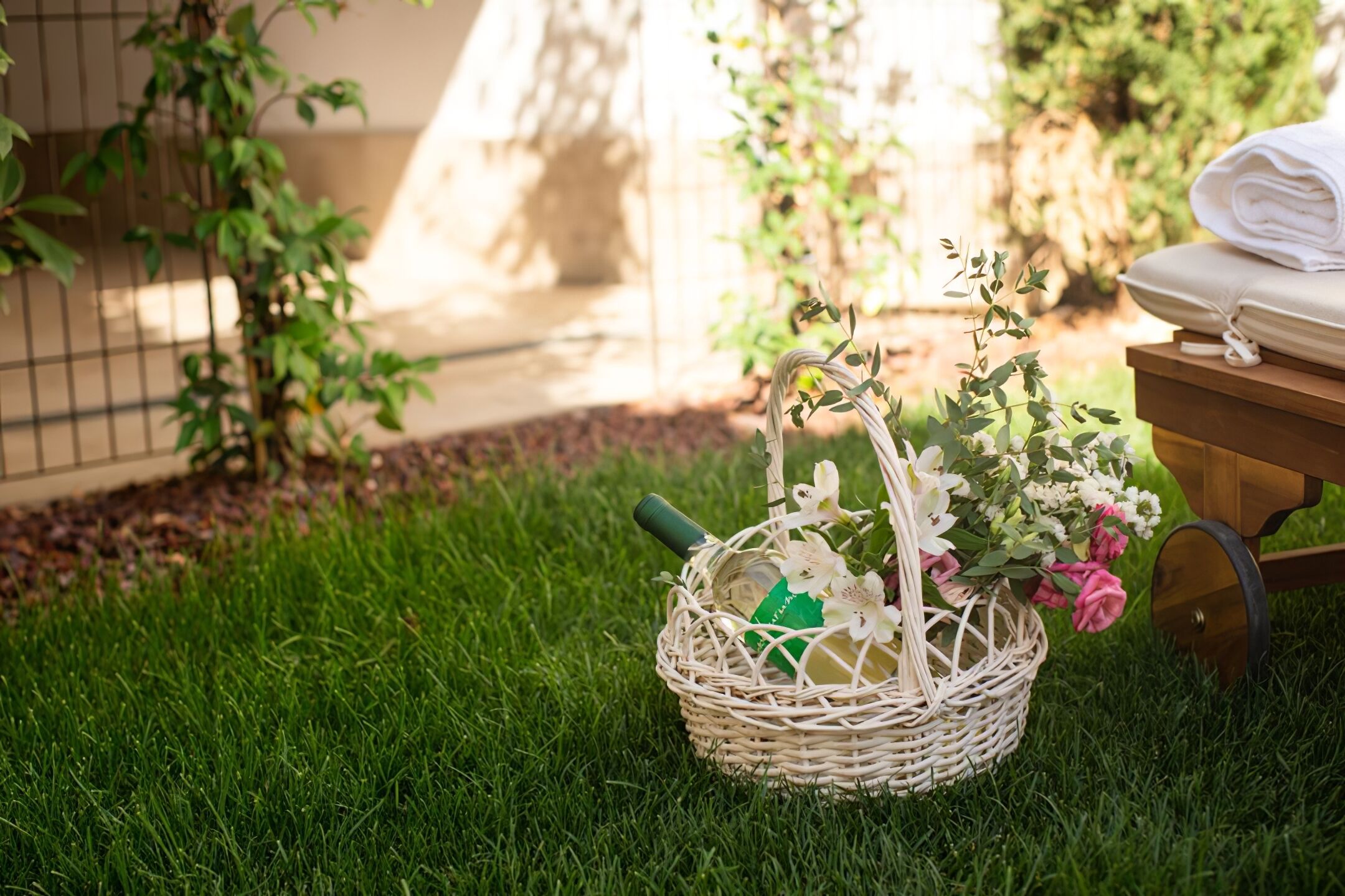 Un panier en osier contenant des fleurs et une bouteille, placé sur une pelouse, à côté d’une charrette en bois sur laquelle sont pliées des serviettes.