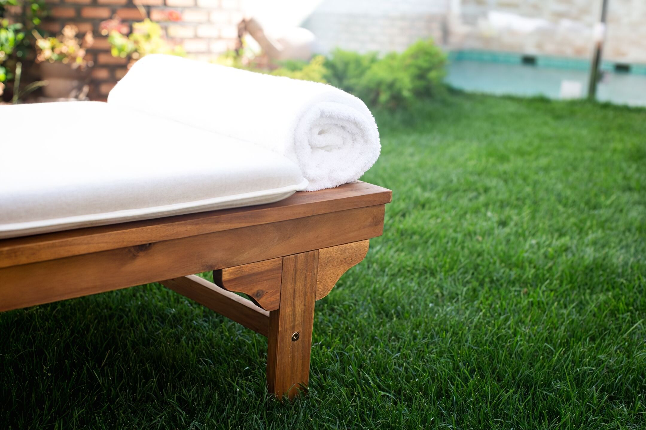 A wooden bench with a rolled white towel on it, set on a grassy lawn.