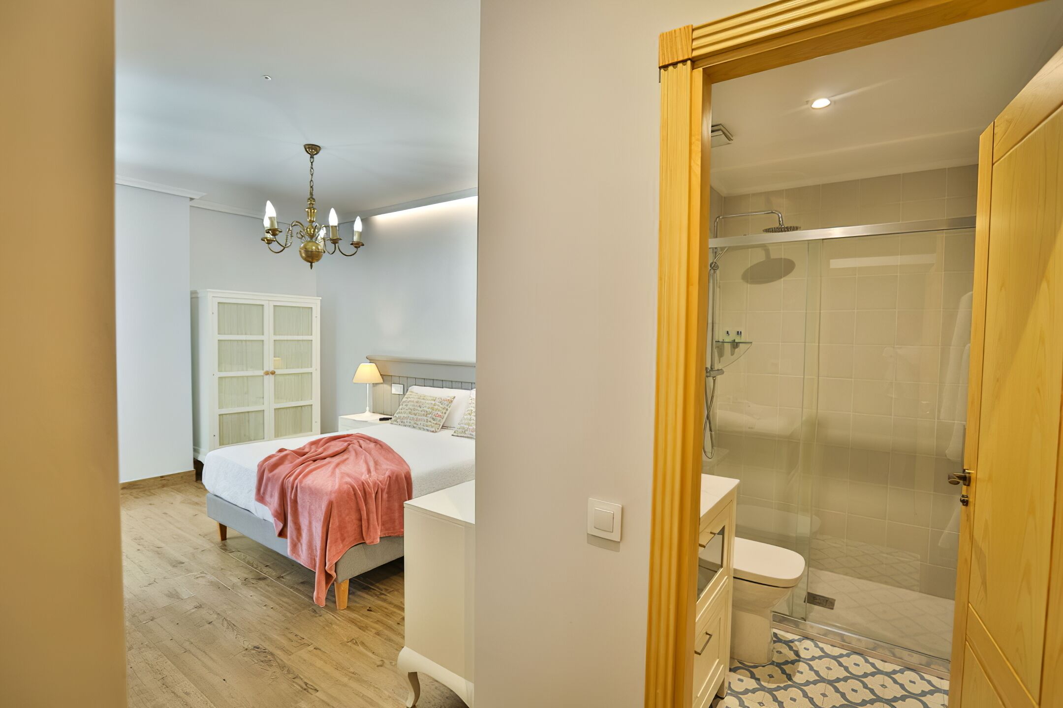 A bedroom with a bed, bedside table, and a nightstand. There is a bathroom with a shower, toilet, and sink.