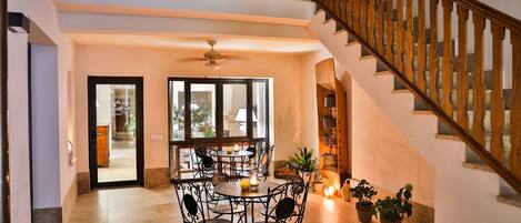 A spacious dining area with a round table and chairs, a staircase with wooden railings, and potted plants.