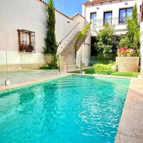 Una piscina con agua cristalina azul, rodeada por un edificio blanco con balcón y una escalera que lleva a una puerta.