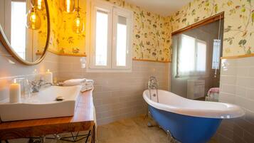 Un baño con lavamanos blanco, bañera azul y papel tapiz con motivos florales.