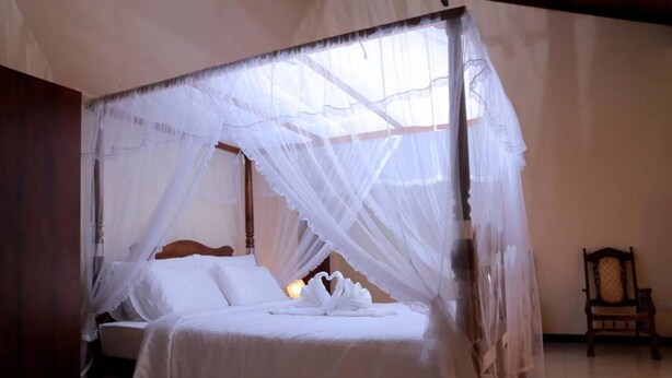 Una cama con dosel y cortinas, con ropa de cama blanca y una disposición de toallas en forma de corazón.