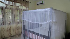 Una habitación con una cama cubierta por una mosquitera, cortinas con estampado de árbol y un equipo de aire acondicionado en la pared.