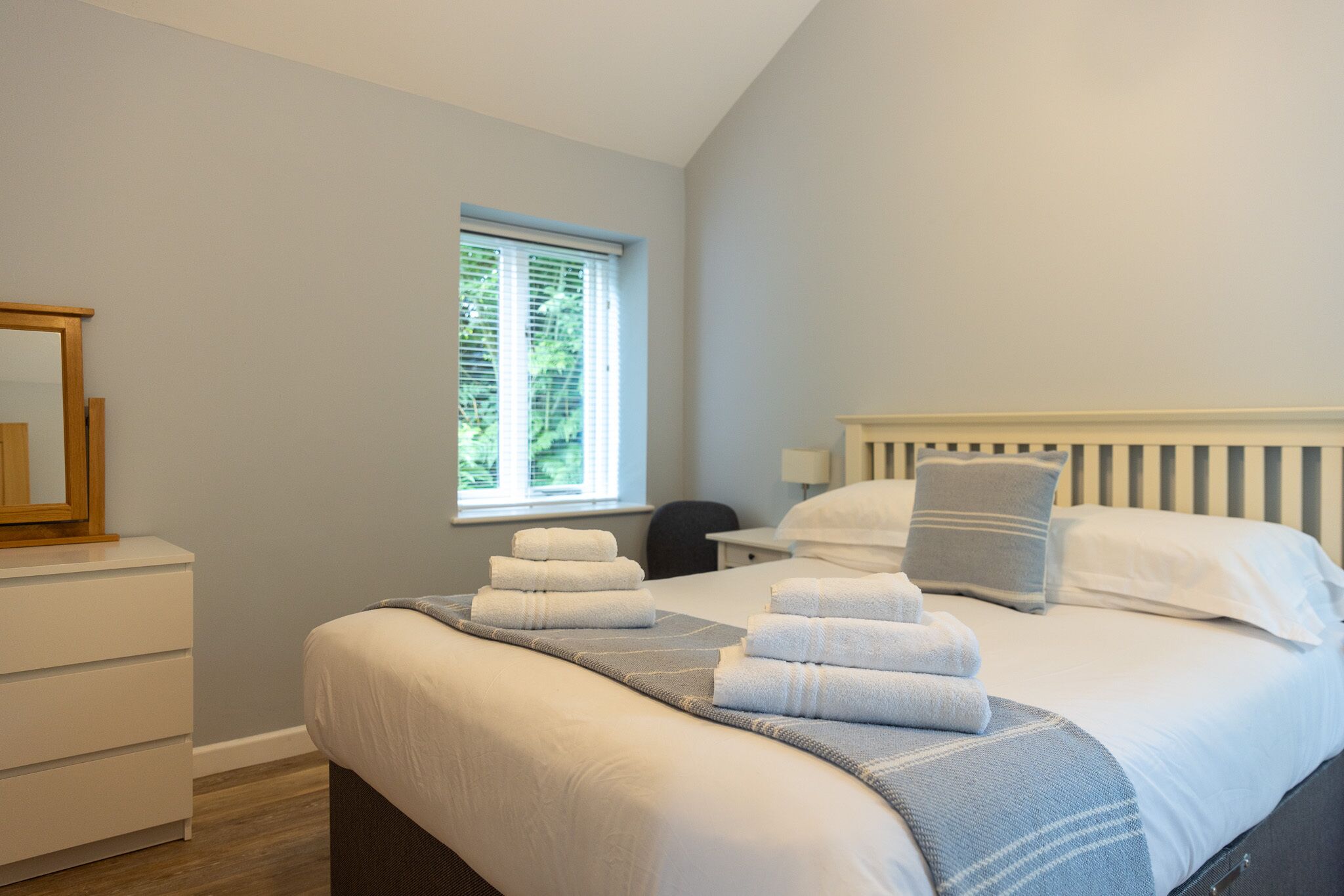 A bedroom with a bed, a nightstand, a window, and a mirror.