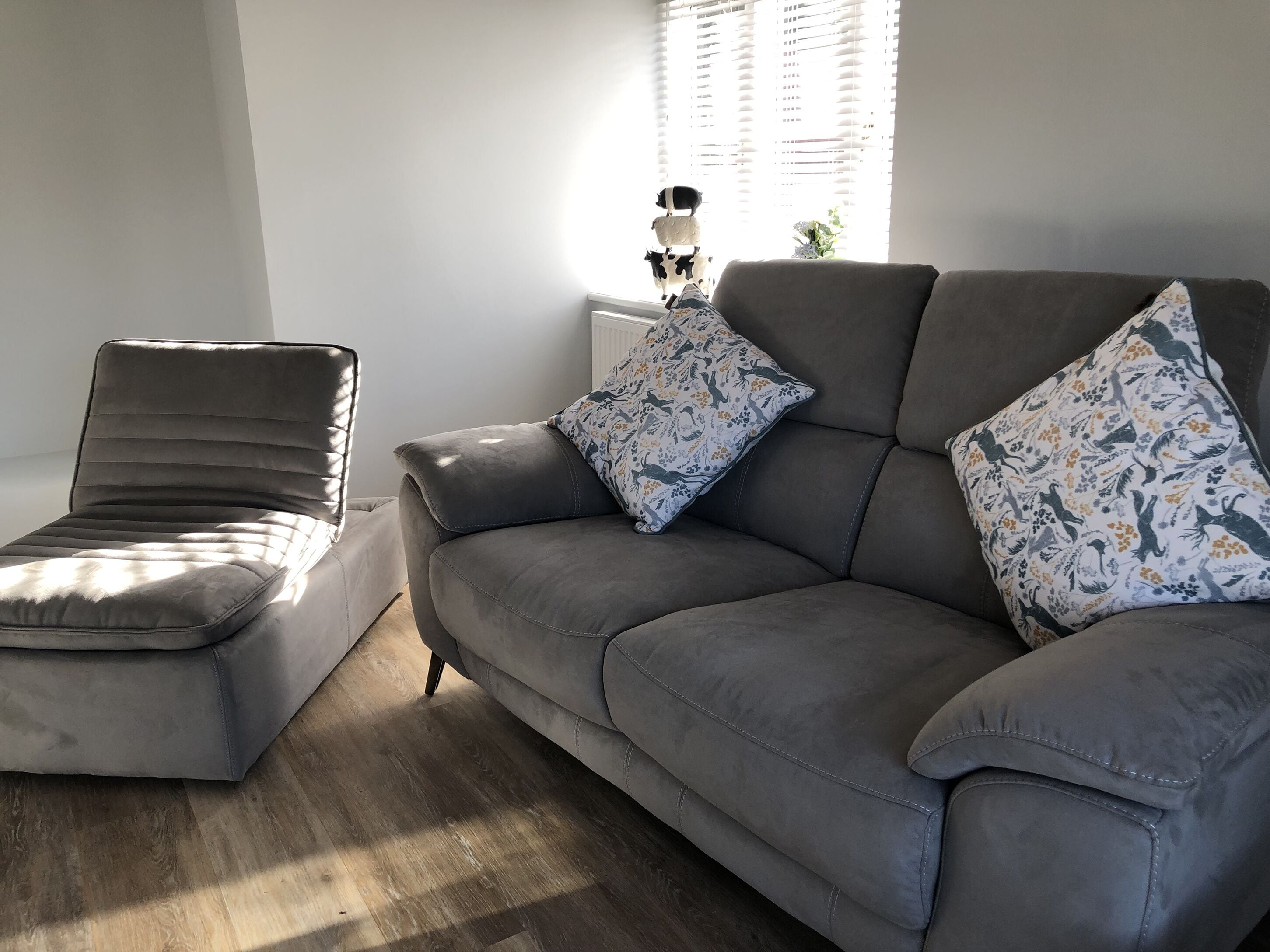 A modern living room with a grey sofa and a matching armchair, both with patterned cushions.