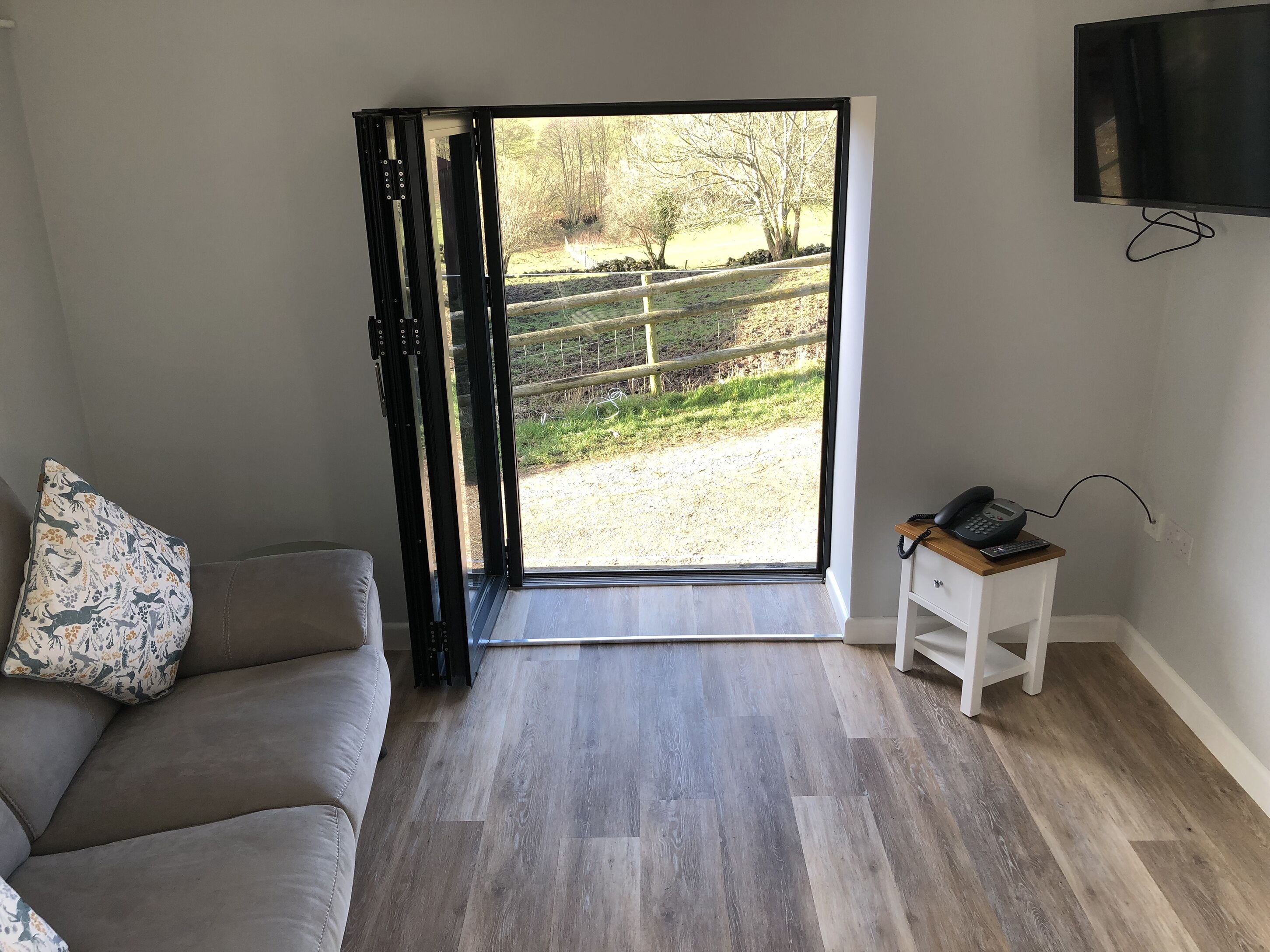 A room with a sofa, a small table with a phone, and a TV on the wall.