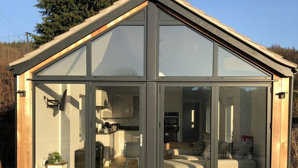 A modern glass house with a kitchen and living area visible through the large glass doors. - Welsh Marches at Upper Glyn Farm (Chepstow)