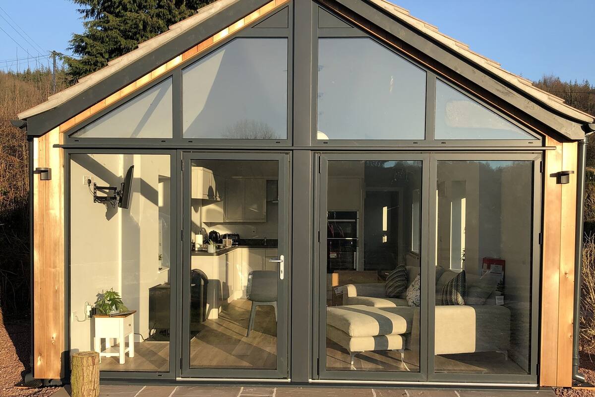 A modern glass house with a kitchen and living area visible through the large glass doors.