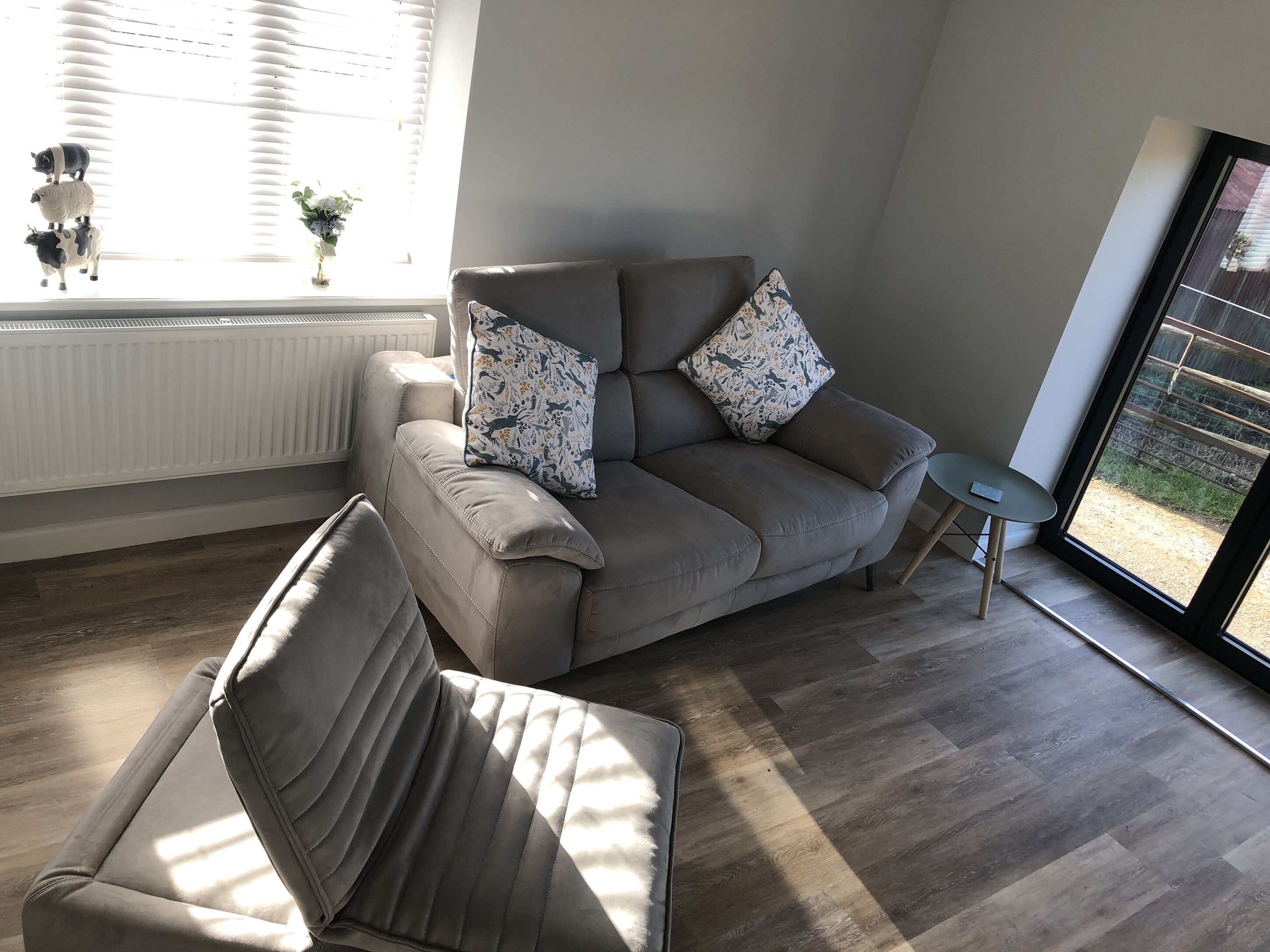 Un salon moderne avec un canapé gris, un fauteuil assorti et des coussins à motifs. Une petite table avec une télécommande se trouve à côté du canapé.