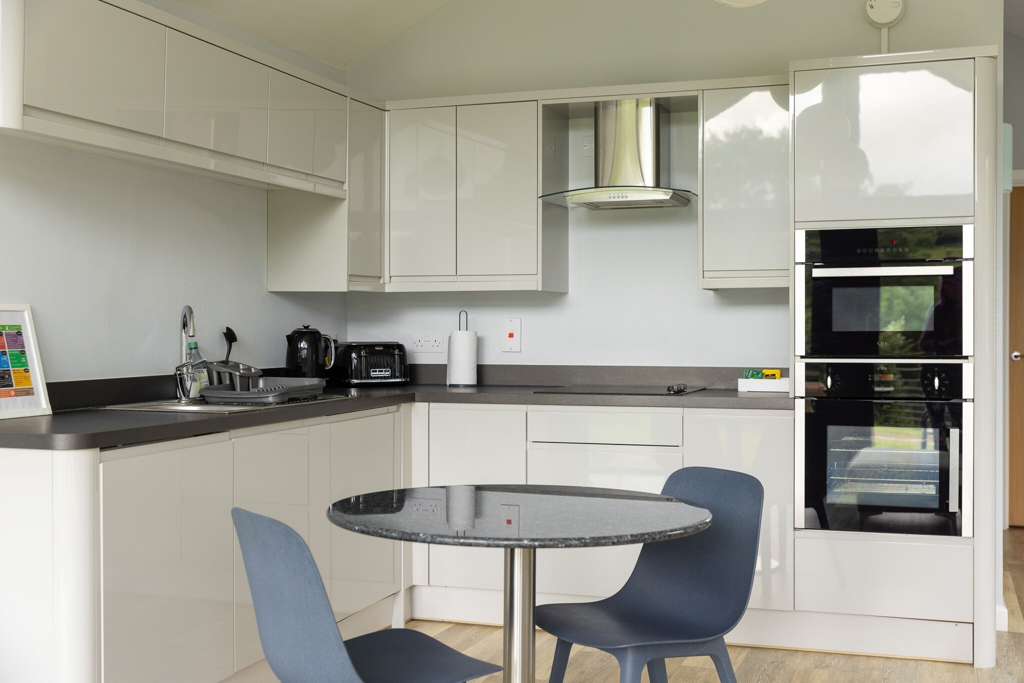 A compact kitchen with white cabinets, a built-in oven, a coffee maker, and a small dining table with chairs.