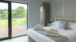 A bedroom with a large bed, a view of a green landscape, and a white headboard. - Welsh Marches at Upper Glyn Farm (Chepstow)
