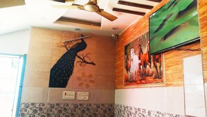 Une chambre d’hôtel avec un ventilateur de plafond, une fresque représentant un paon, un téléviseur et des carreaux décorés.