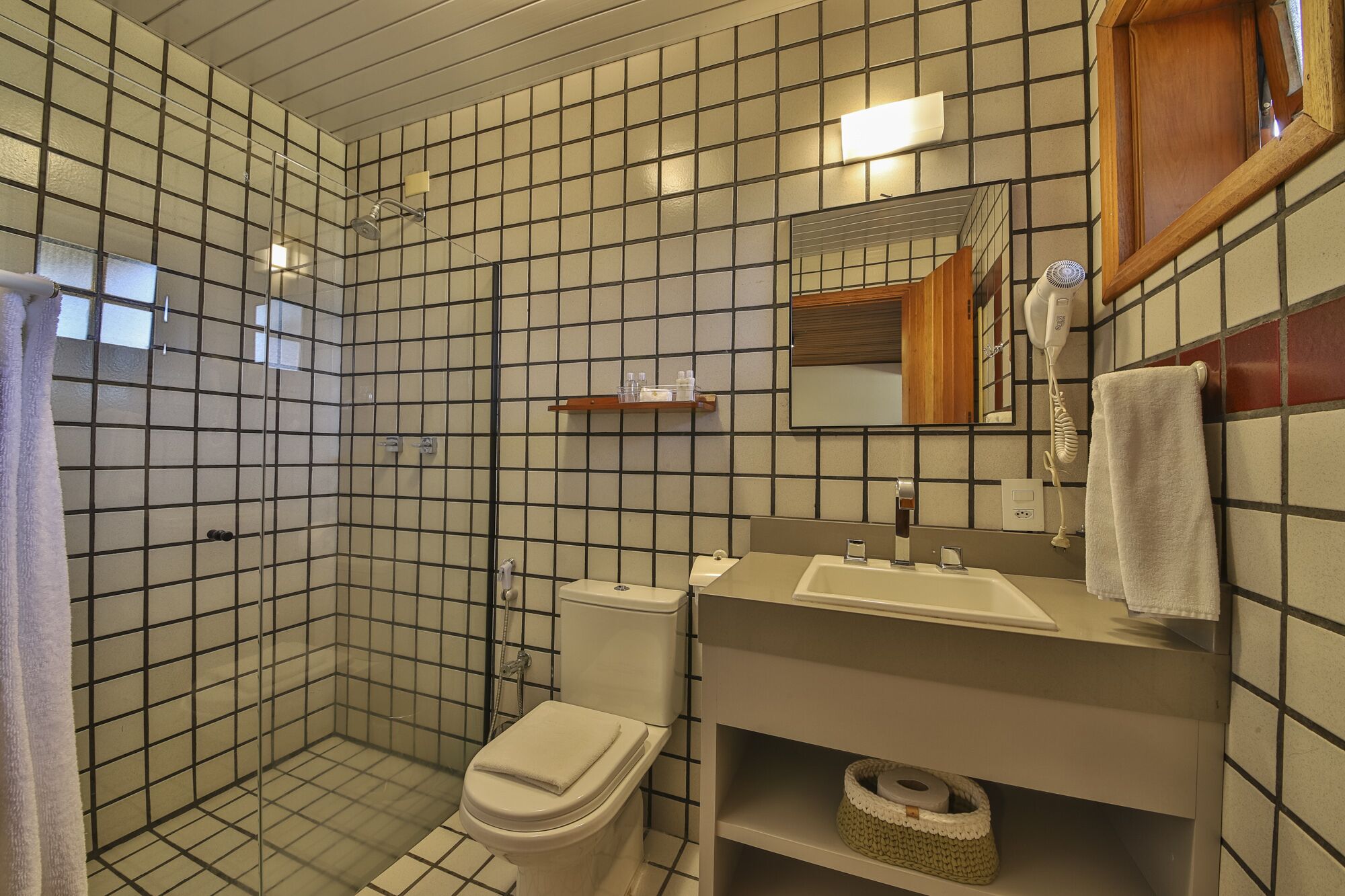 A bathroom with a tiled floor, a toilet, a sink, a mirror, and a shower area.