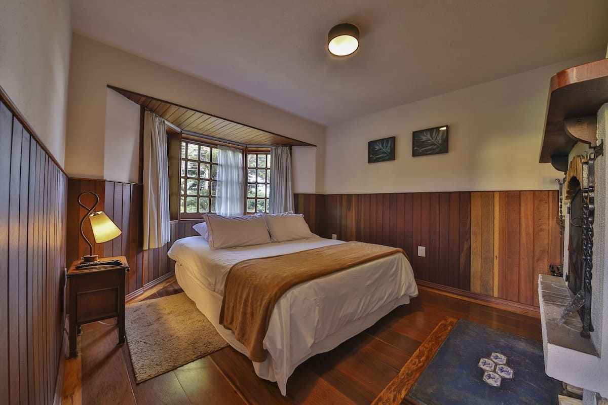 Une chambre à coucher avec un lit en bois, une table de chevet avec une lampe, une fenêtre avec des rideaux et un tableau accroché au mur.